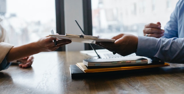 person passing a clipboard and pen over to someone across a desk)